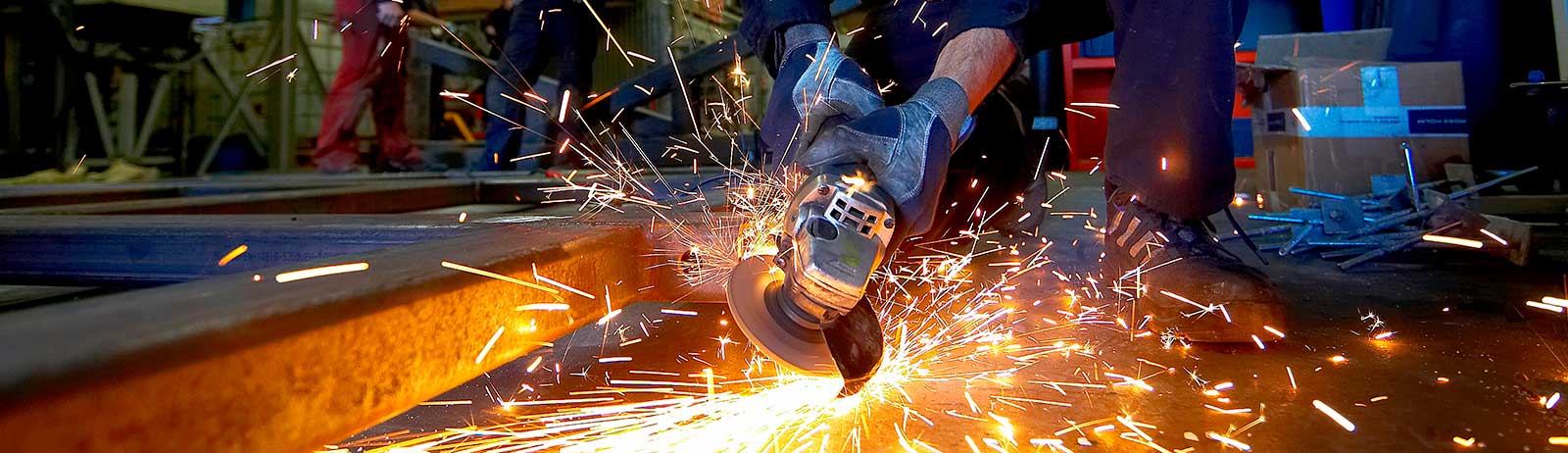 En håndværker bruger en vinkelsliber på en metalkonstruktion, og gnisterne flyver ud til alle sider. 