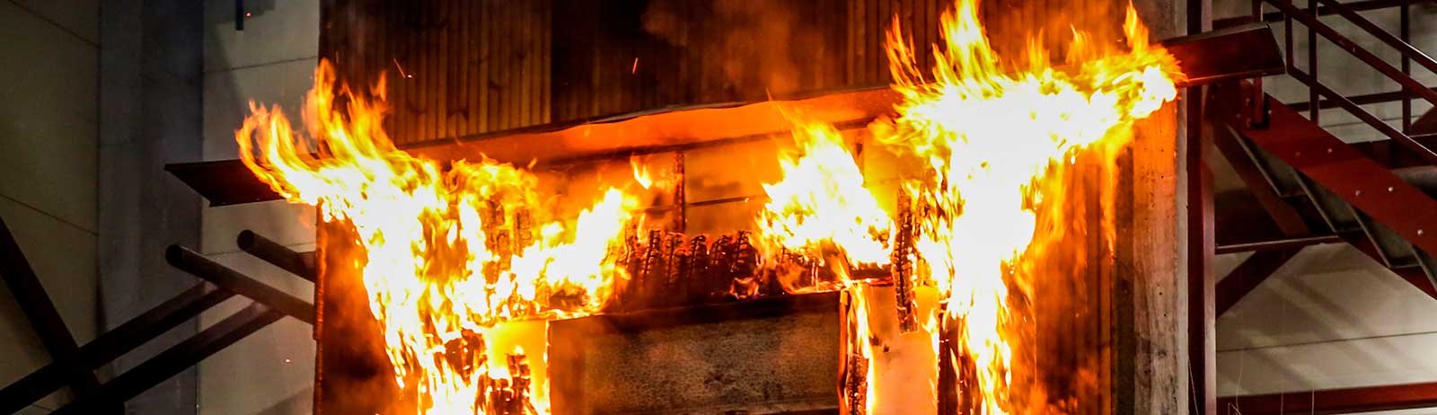 Nærbillede af kraftige flammer, der spreder sig over en træfacade under brandtest.