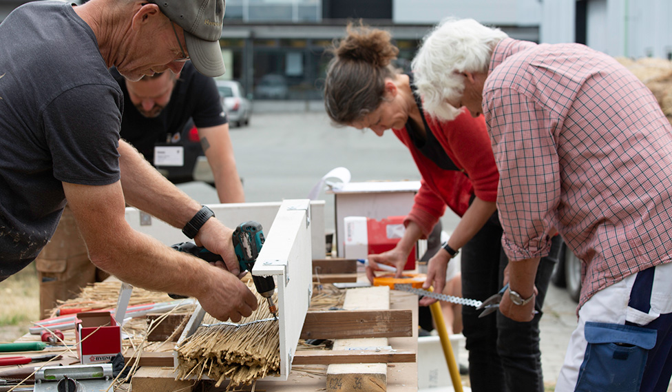Team bygger konstruktionselement af strå og ler, der illustrerer forskning i biobaserede materialer, brandsikkerhed og bæredygtigt byggeri.