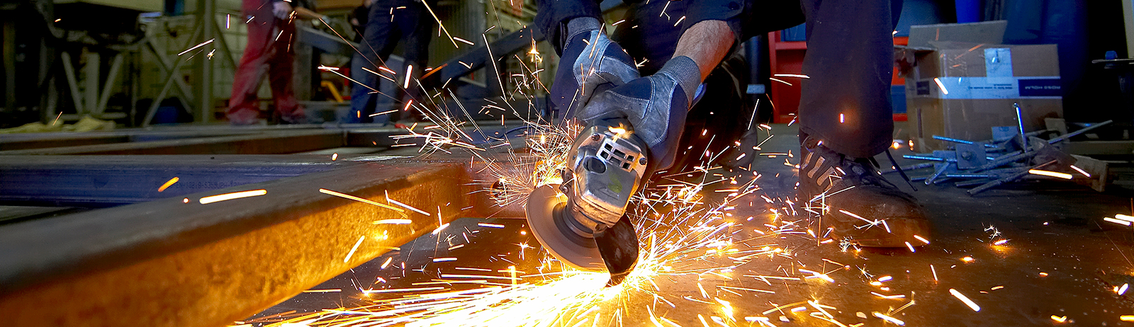 En håndværker bruger en vinkelsliber på en metalkonstruktion, og gnisterne flyver ud til alle sider.