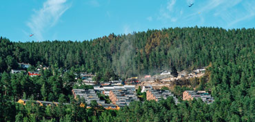 Røg stiger op fra Krokstadelva i Norge efter storbrand, der illustrerer hurtig brandspredning i træhuse på en skråning, skovterræn og beredskabsindsats.