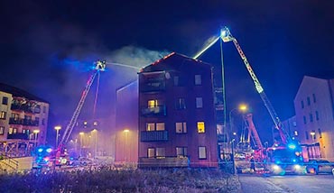 To drejestiger sprøjter vand på taget af et brændende etagebyggeri i Upplands-Bro.