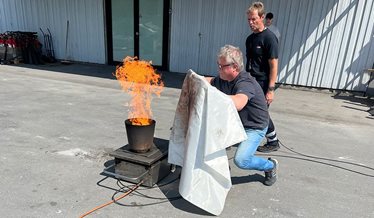 En mand prøver at slukke en brand i en spand, ved hjælp af et brandtæppe