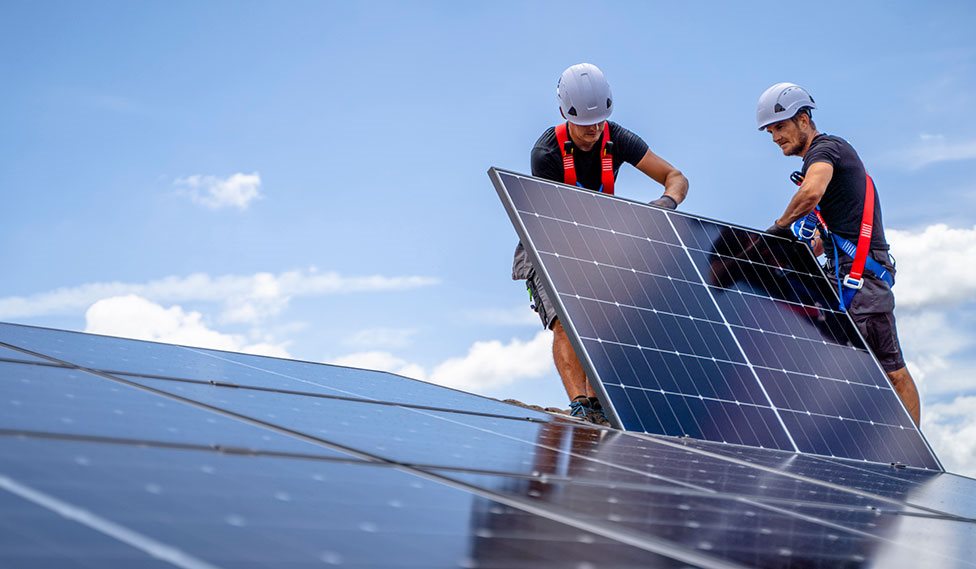 To installatører lægger det sidste solcellepanel på et tag.