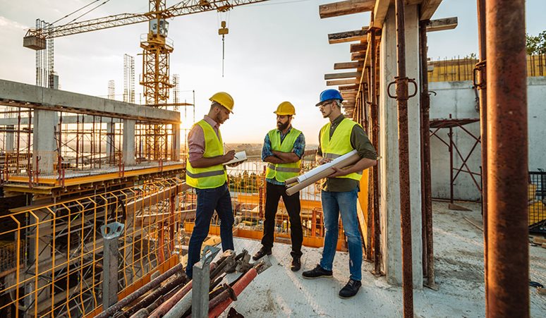 Tre håndværkere står på en byggeplads og snakker.