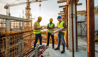 Tre håndværkere står på en byggeplads og snakker.