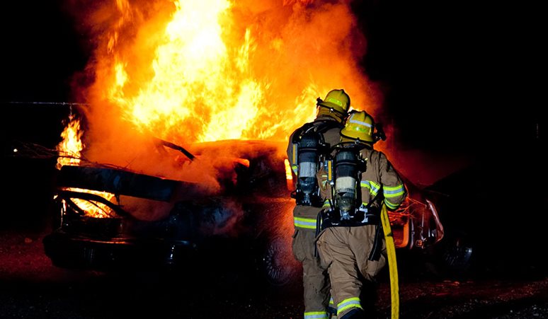 Brandfolk bekæmper kraftig bilbrand med store flammer i mørke omgivelser.